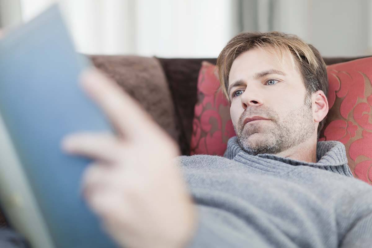 Ein Mann liegt auf einem Sofa und liest ein Buch.