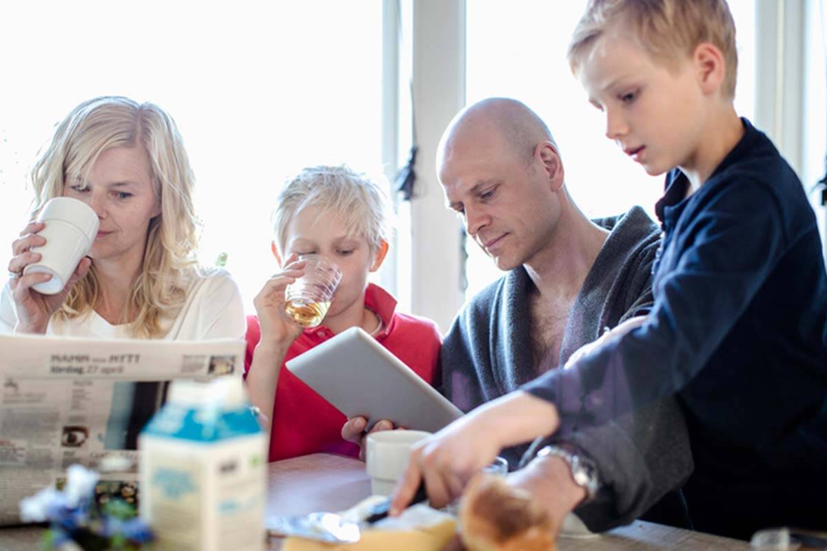 Eine Familie frühstückt zusammen und während die Kinder essen, lesen die Eltern.