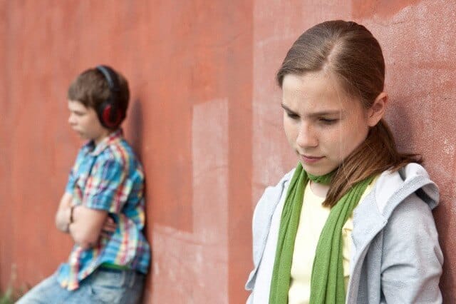 Ein Mädchen und ein Junge stehen voneinander entfernt, beide angelehnt an eine rote Wand.