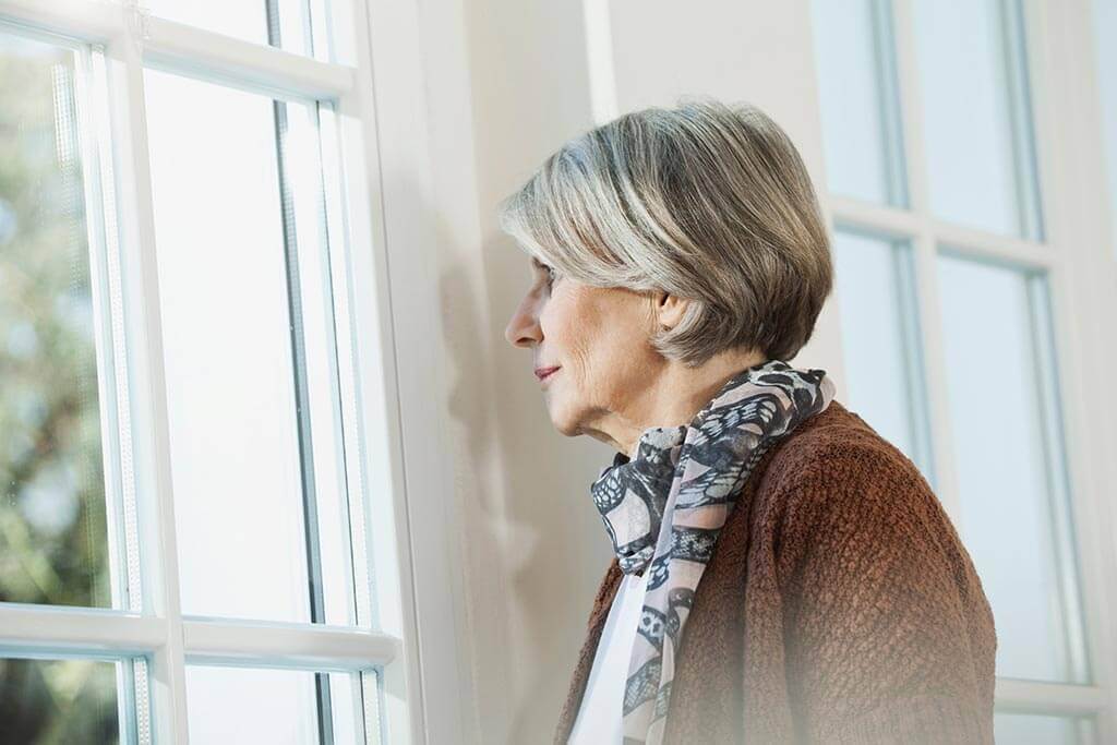 Frau schaut aus dem Fenster in ihren Garten.