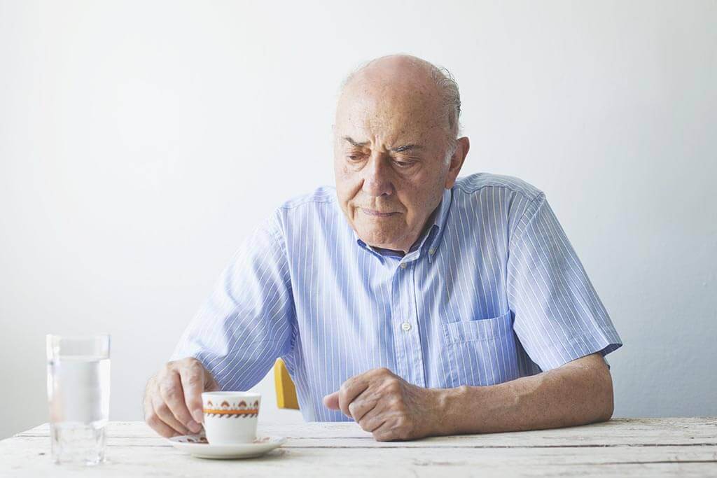 Älterer Herr sitzt an einem Tisch und trinkt eine Tasse Kaffee.