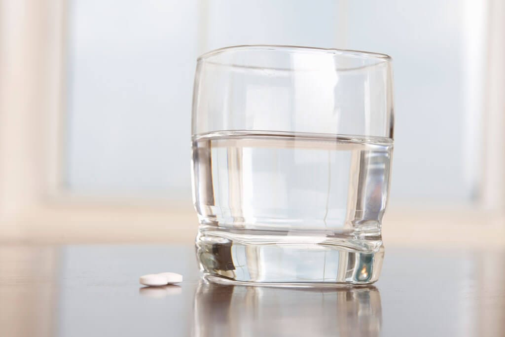 Ein Glas Wasser steht neben einigen Tabletten auf dem Tisch