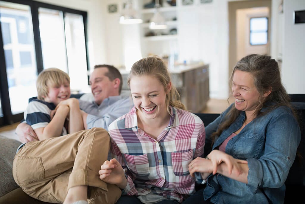 Eine Familie sitzt zusammen auf dem Sofa und lacht.